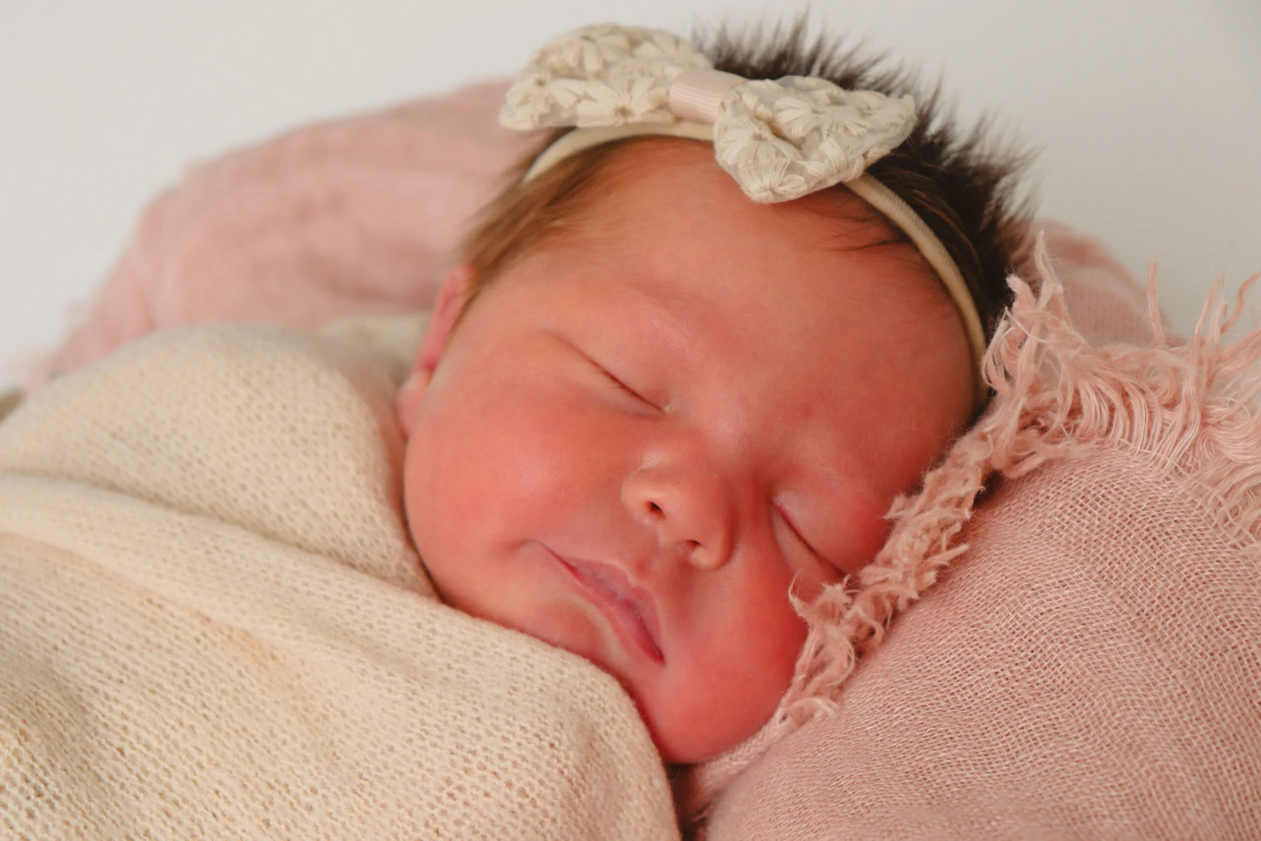 A newborn baby girl. She is wearing a white bow on her head