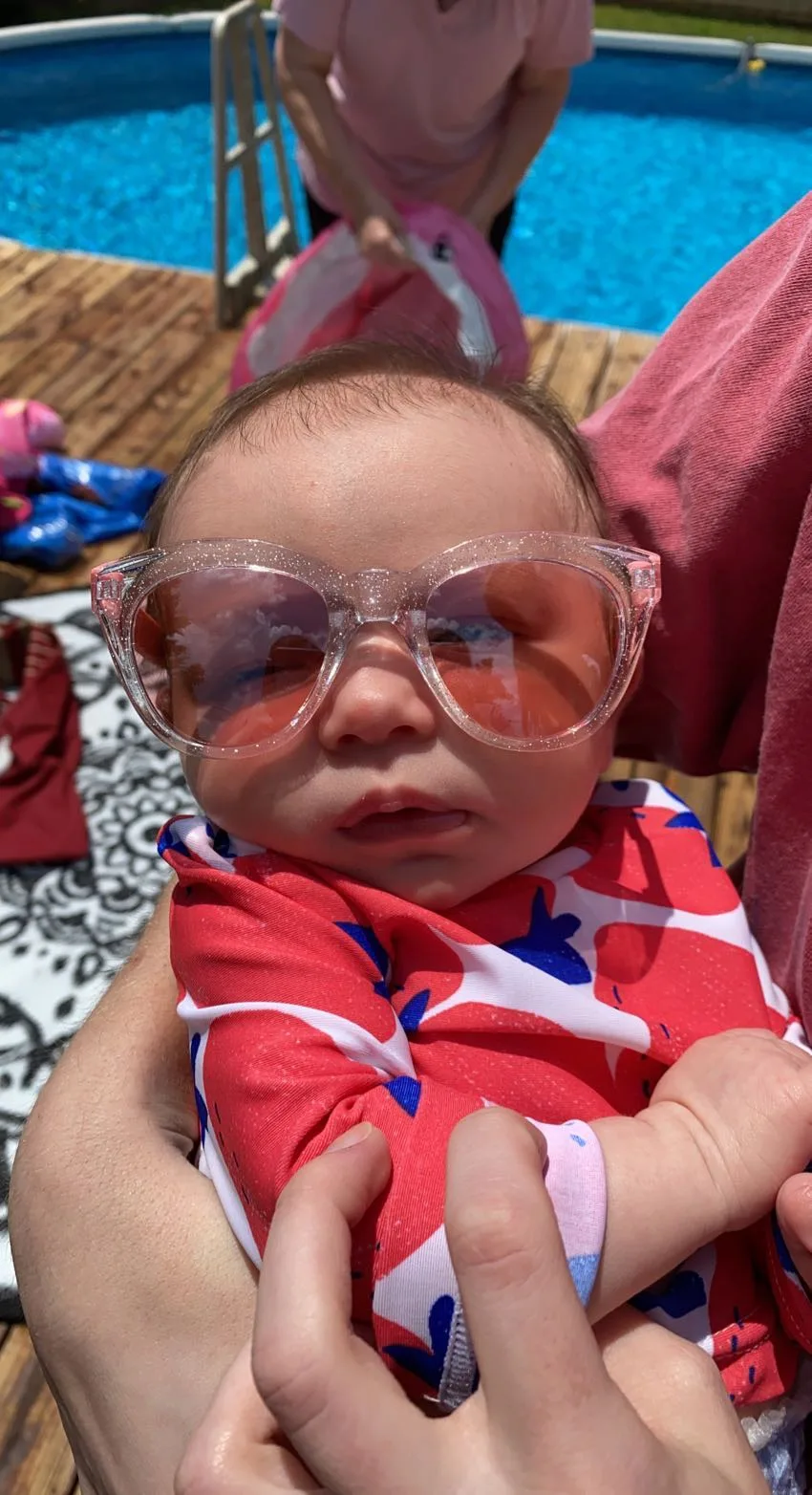 A baby by the pool wearing sparkly sunglasses