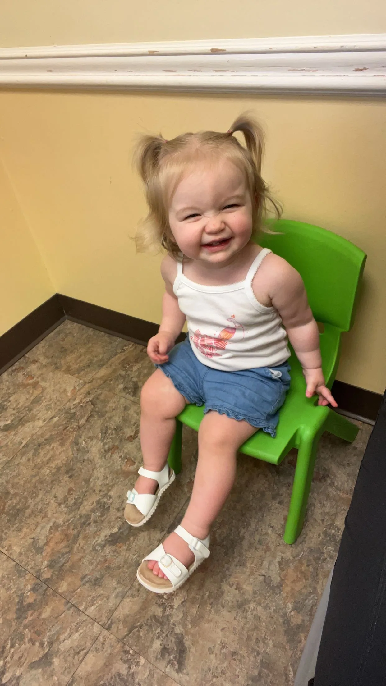 a little girl sits in a green plastic chair smiling at the camera 