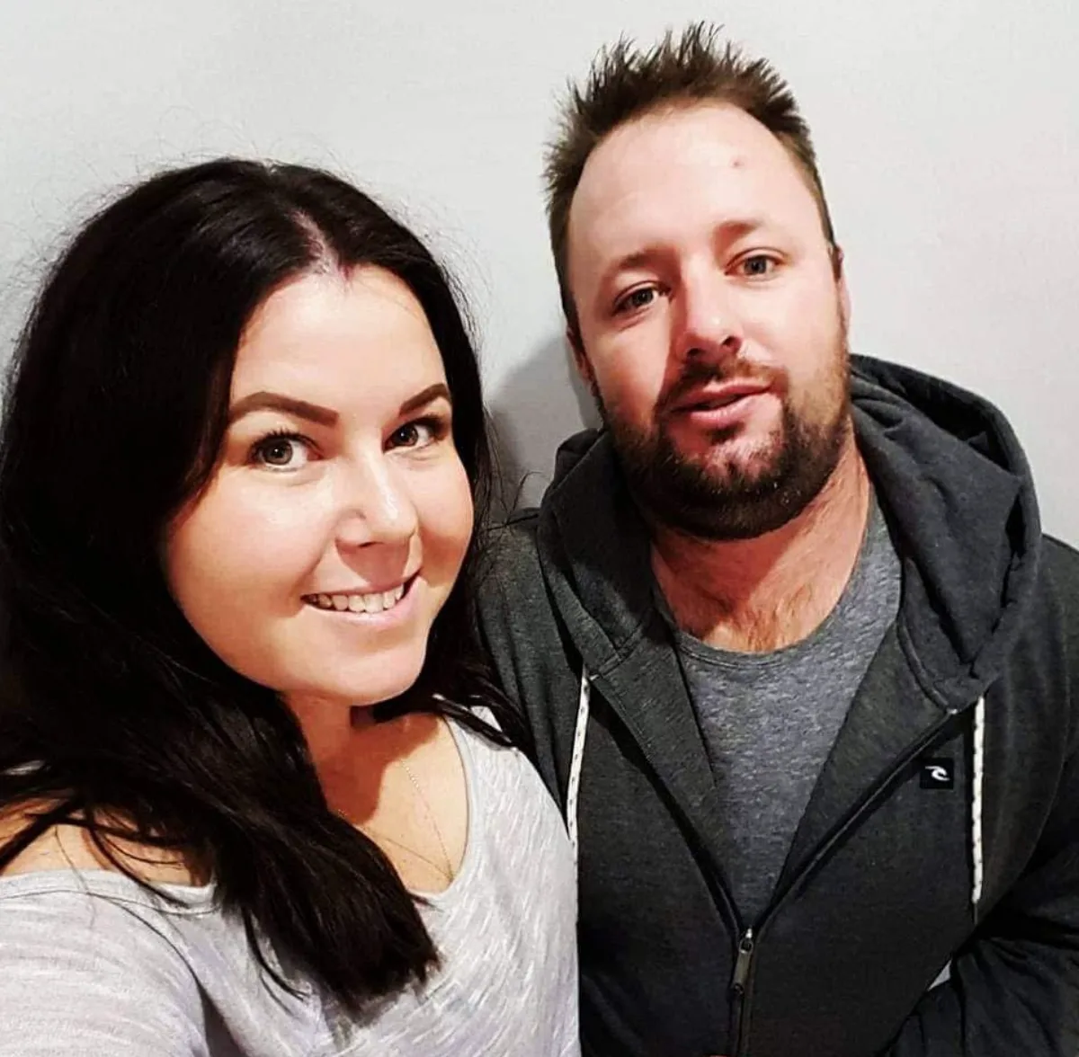 Image of husband and wife smiling, she is wearing a grey top and he is wearing a charcoal hoodie