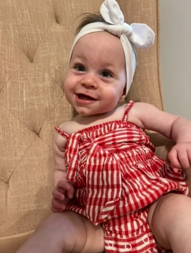 Image of baby girl wearing read and white striped onesie and white bow headband