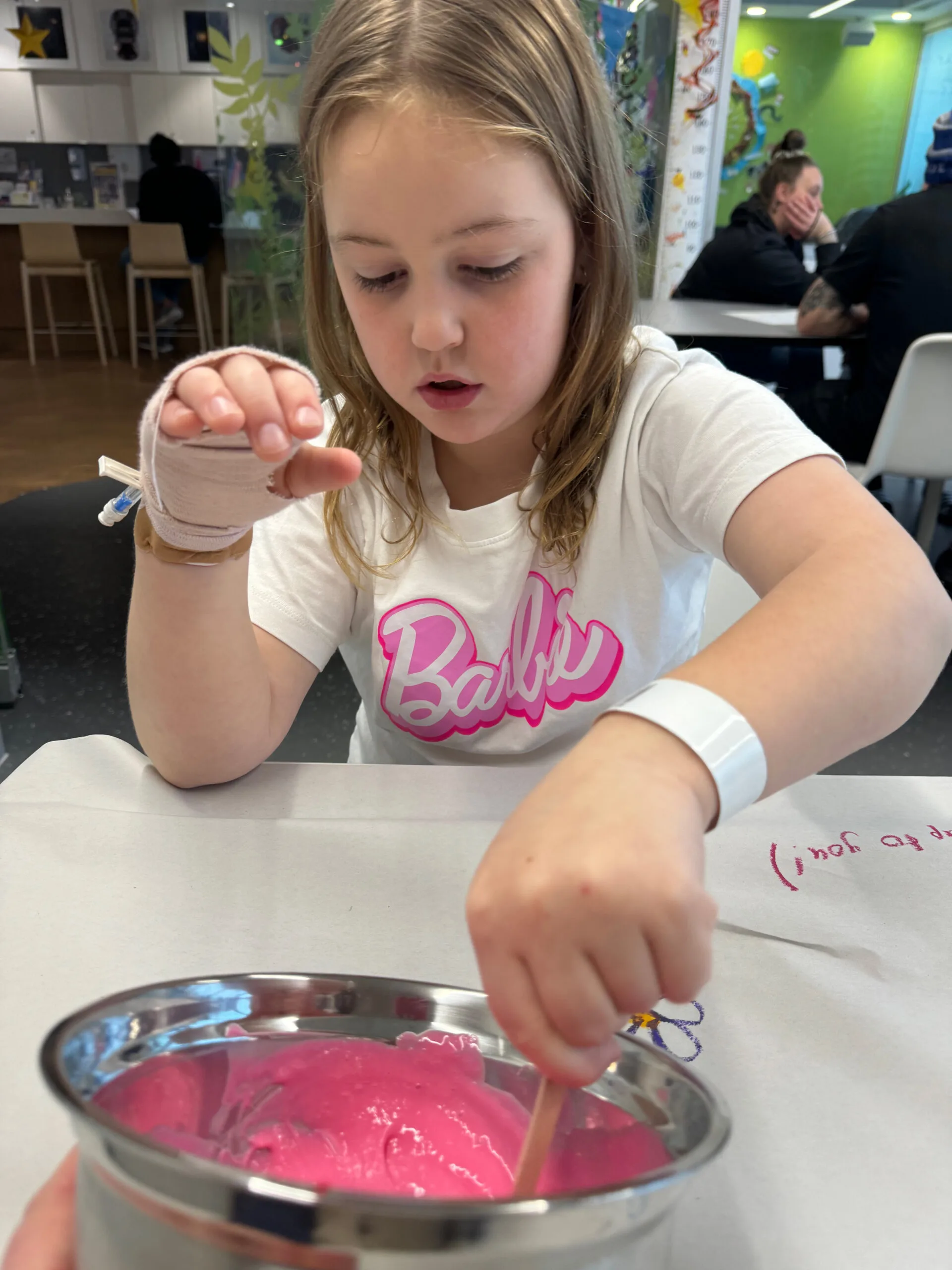 A young girl wearing a barbie tshirt she has a hospital bracelet on and is making pink slime