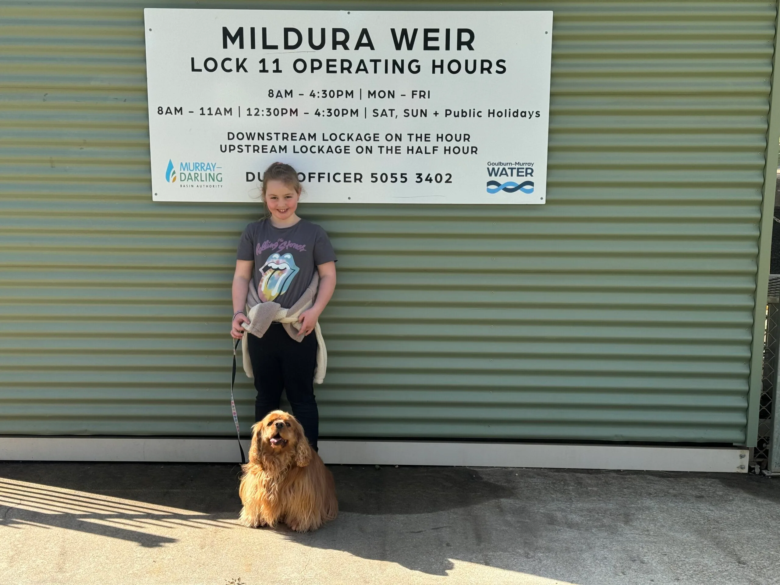 A young girl standing in front of a green wall with her small brown dog