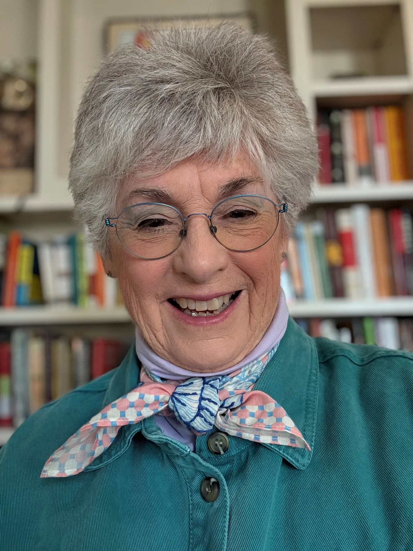 woman in front of bookshelf with white scarf around neck and glasses and blue top 