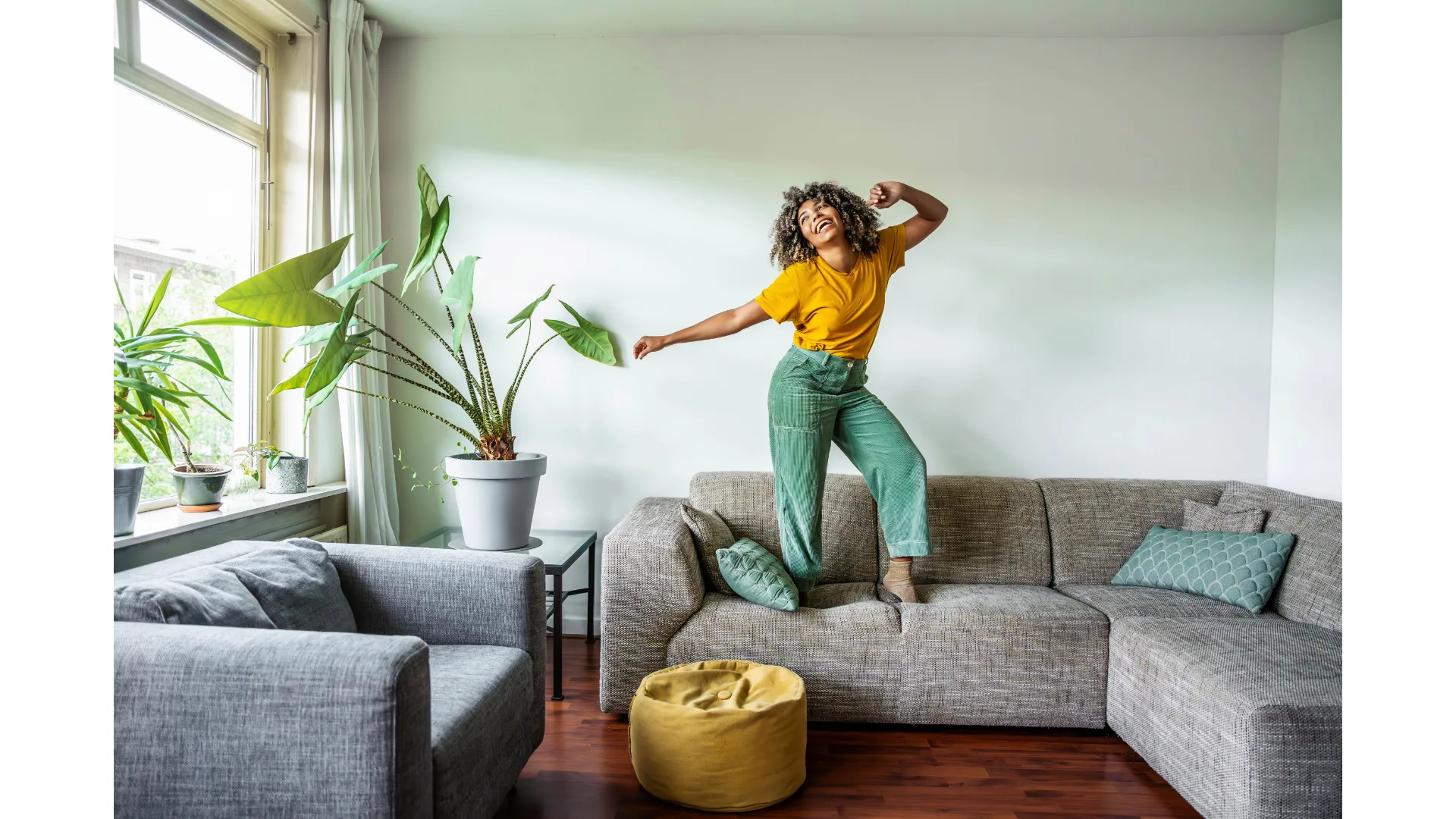 A jovial woman stands on a couch as she dances.