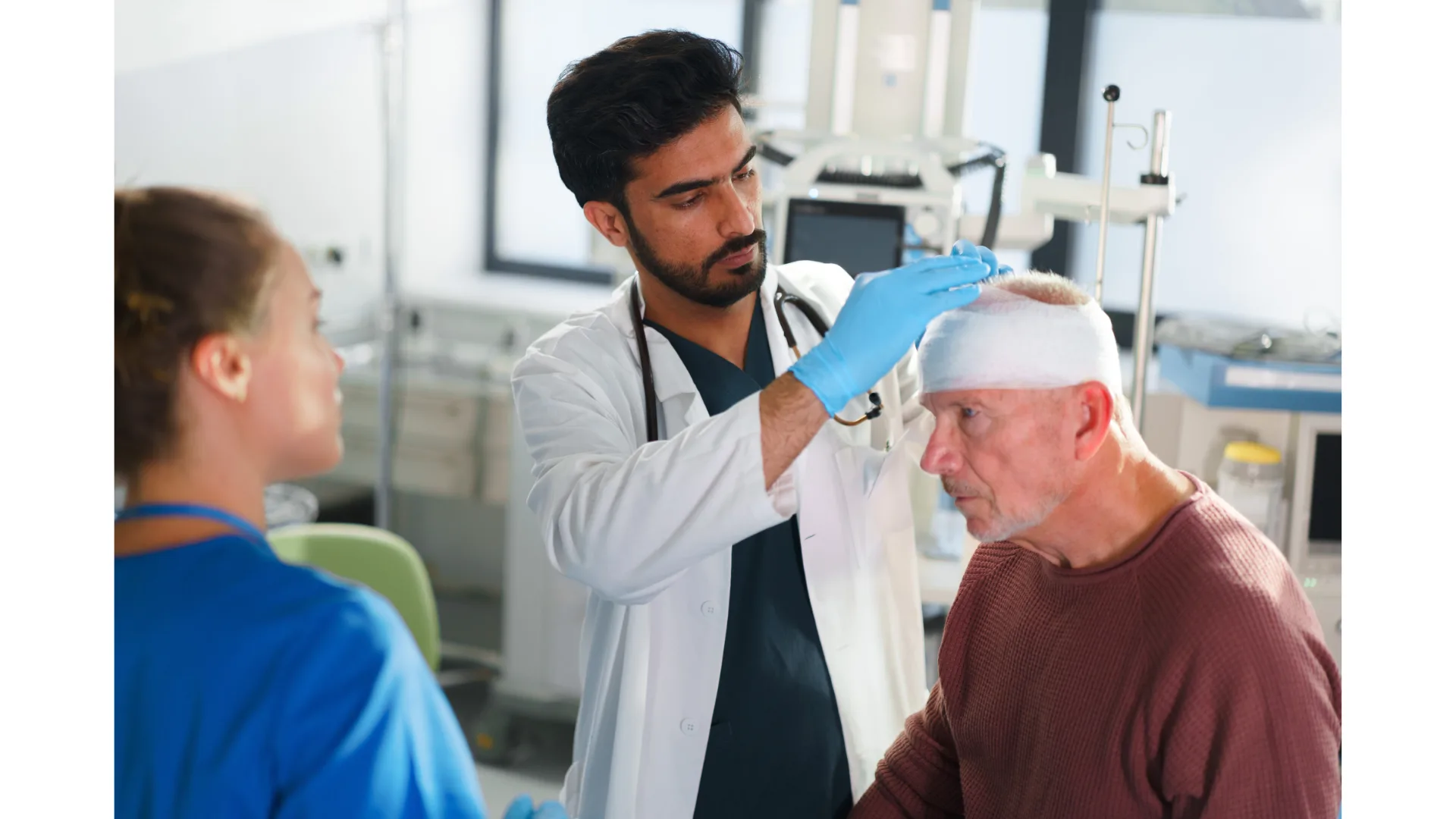 A doctor bandages a man's head as a medical professional watches on.