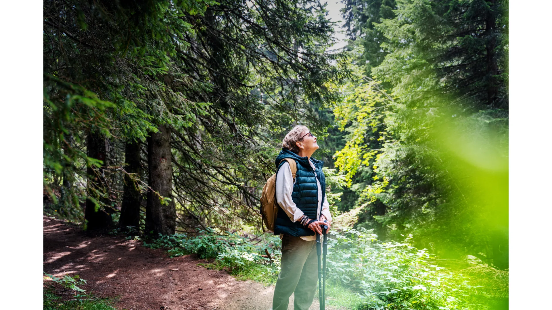 A woman stares upwards while taking a break during a Nordic walk in nature.