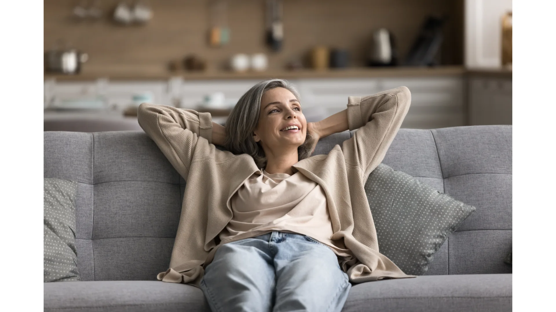 A woman relaxes on a couch with her arms tucked behind her head.