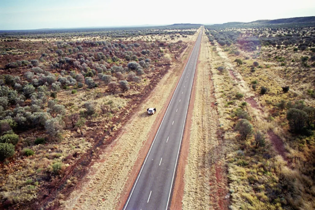 long road in australia outback with grass on either side and white car
