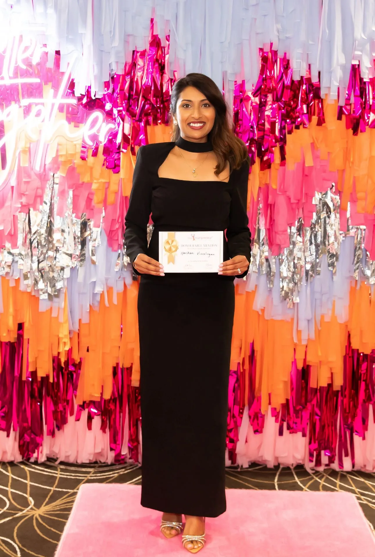 a woman dresses in black in front of a glittery background she is holding a certificate