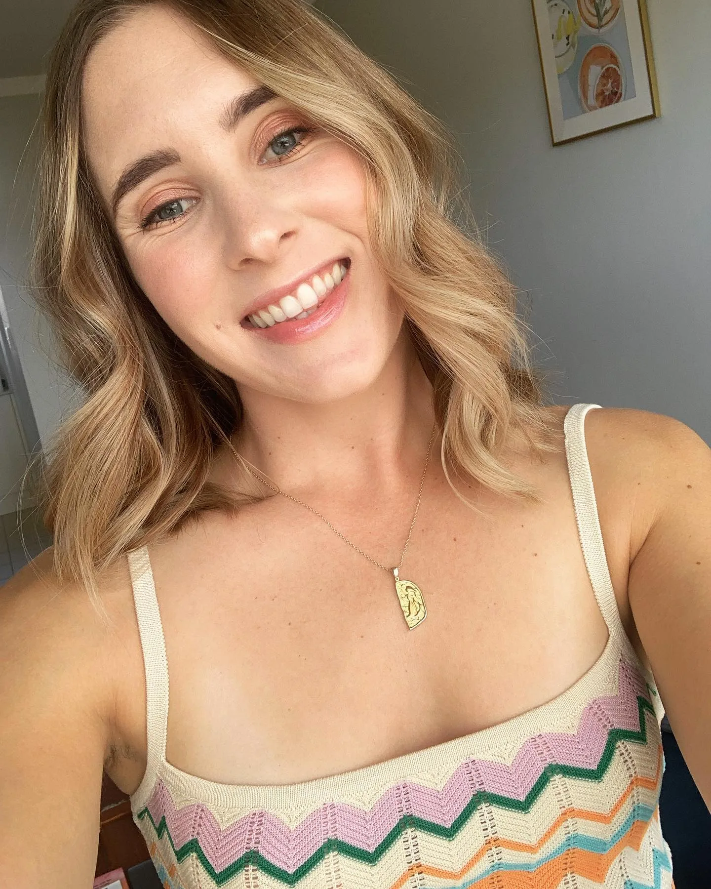 woman wearing rainbow dress, she has her hair blonde curled and is smiling for the camera