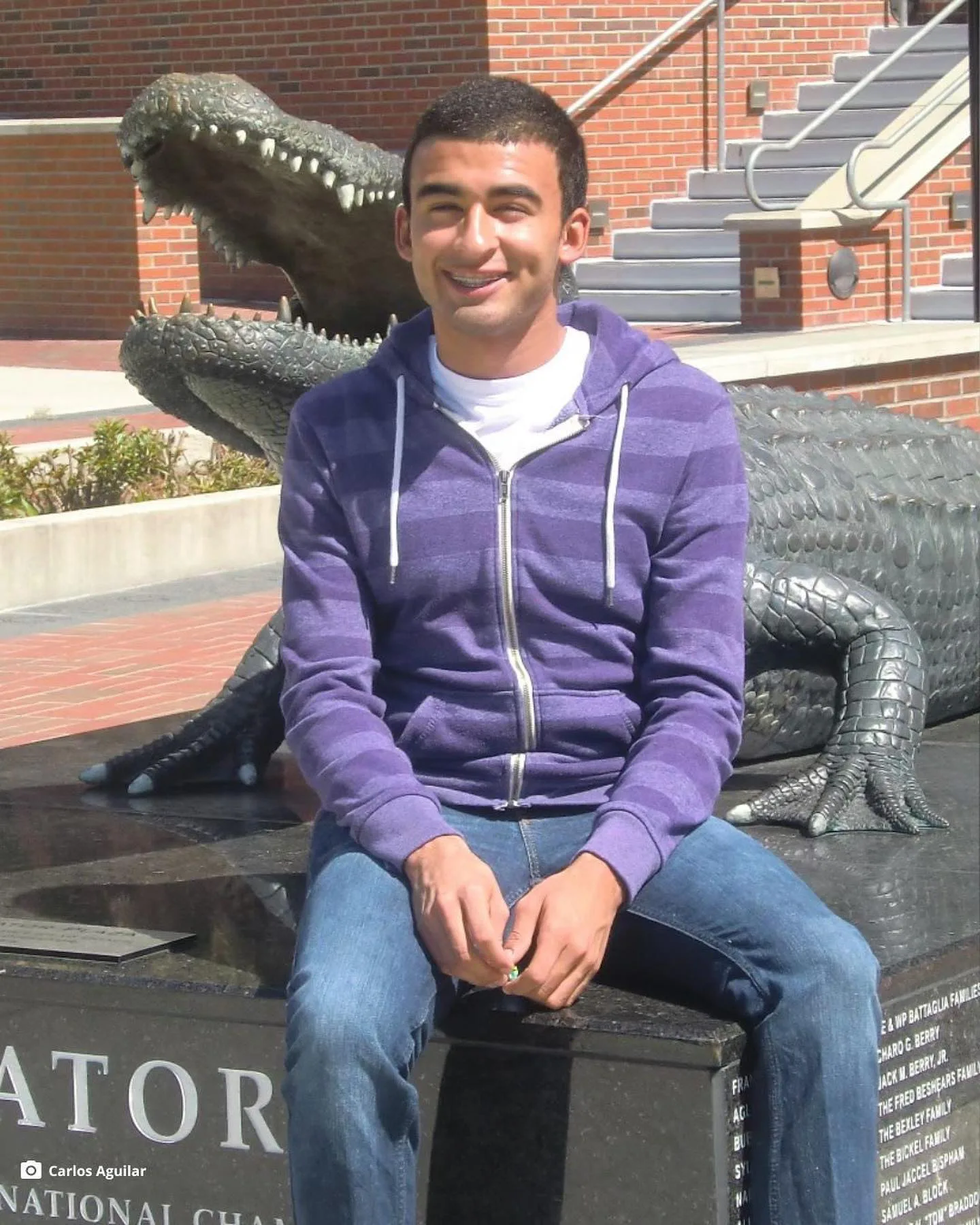 man in purple jumper smiling on a statue