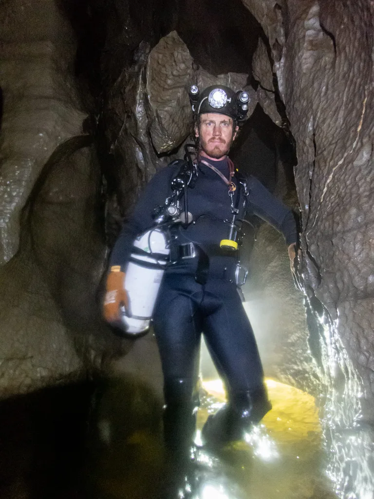 man in black caving gear with headtorch holding oxygen