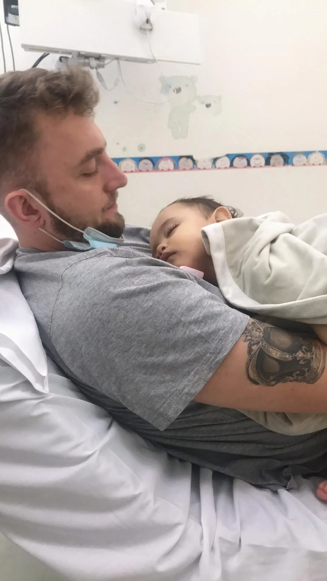 a man in grey cuddles his baby on a hospital bed