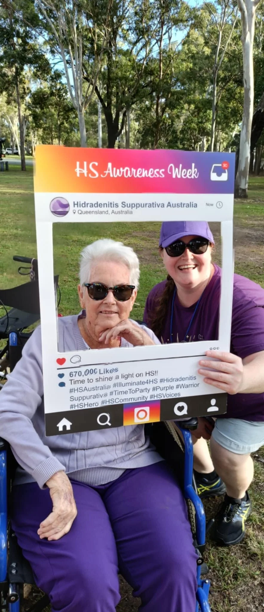 a woman in purple slack and a lilac jumper poses with a woman in a purple cap and t-shirt together they hold a HS Australia sign