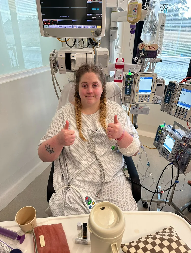 Tess in ICU, after double hip replacement surgery. She is smiling with her thumbs up.