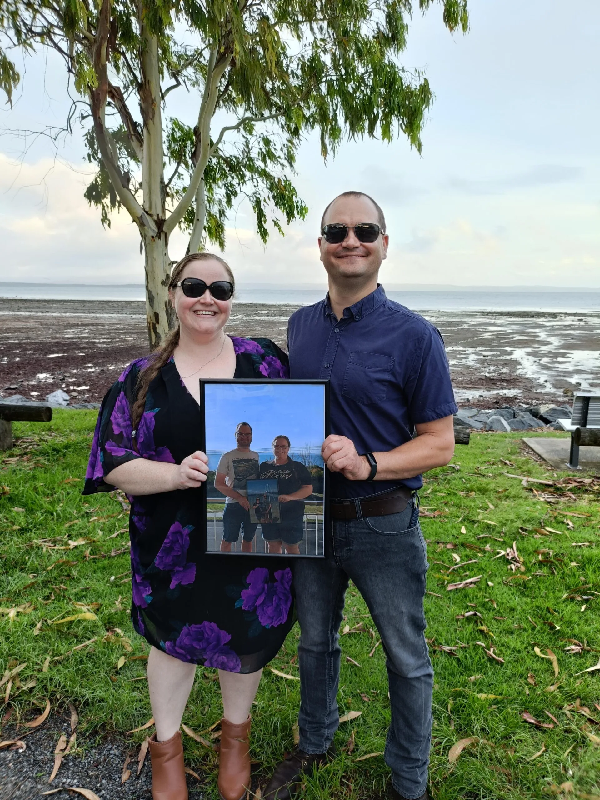 a man and woman stand together holding a photo of themselves