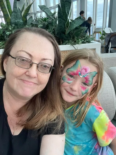 A young girl is wearing a rainbow tye-die top and her mother next to her is wearing a black tshirt