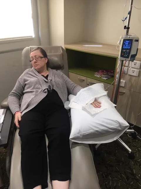 A woman on a grey medical chair, she has an IV of medication in her arm