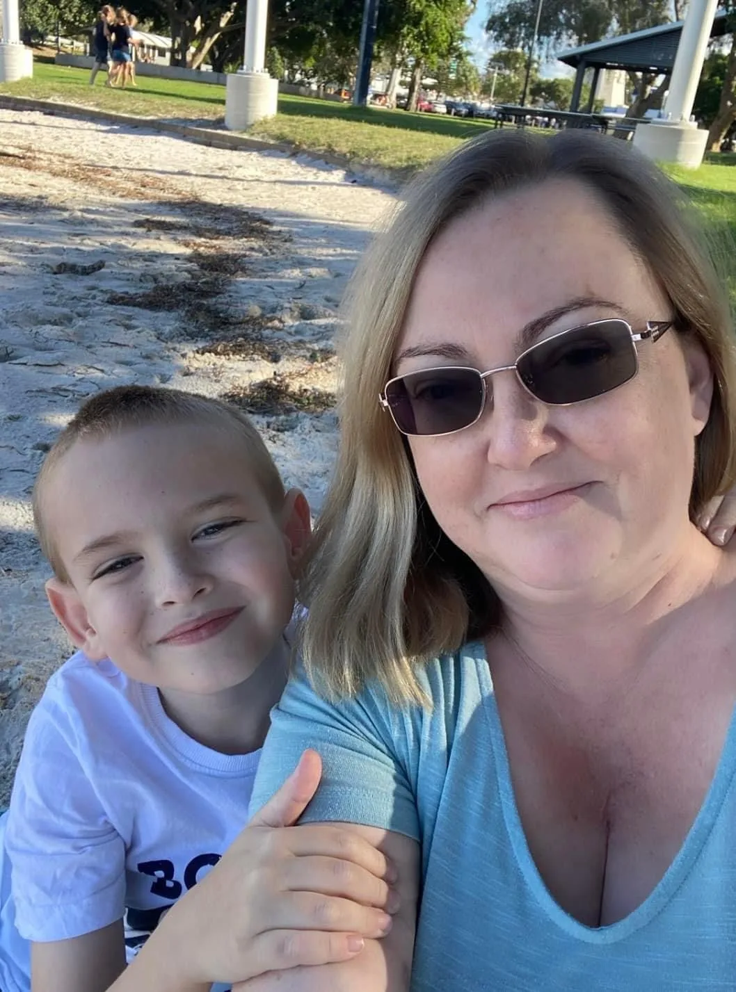 a woman and young son both wearing blue t-shirts arm in arm at the beach