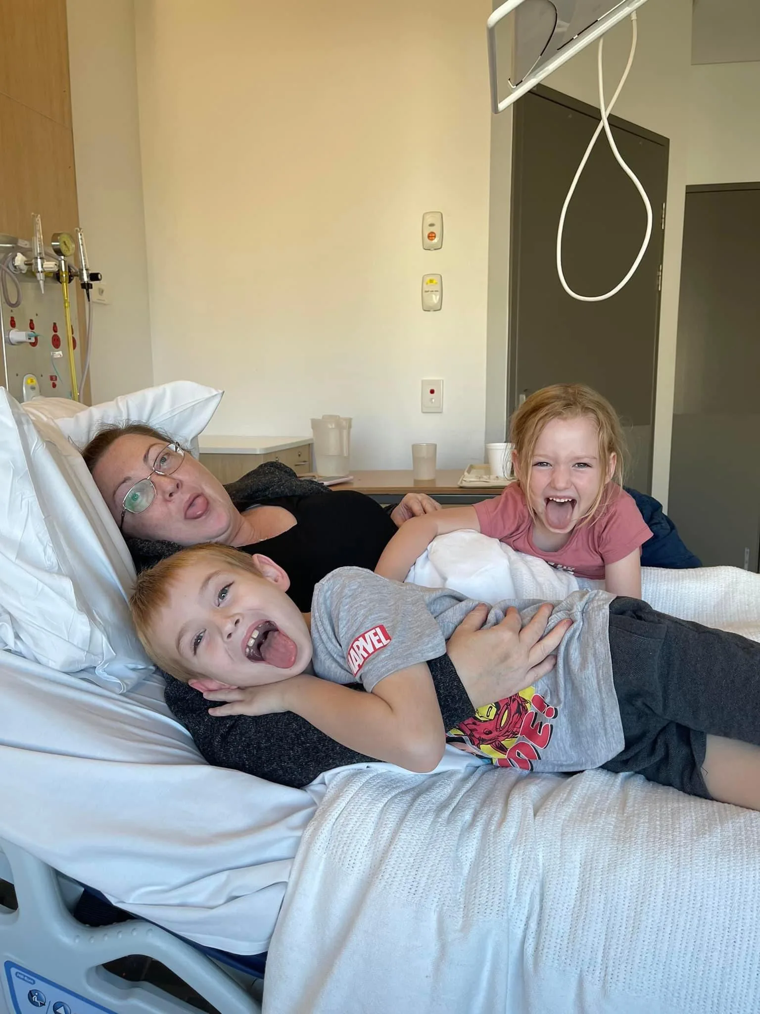 two children cuddle with their mother on the hospital bed