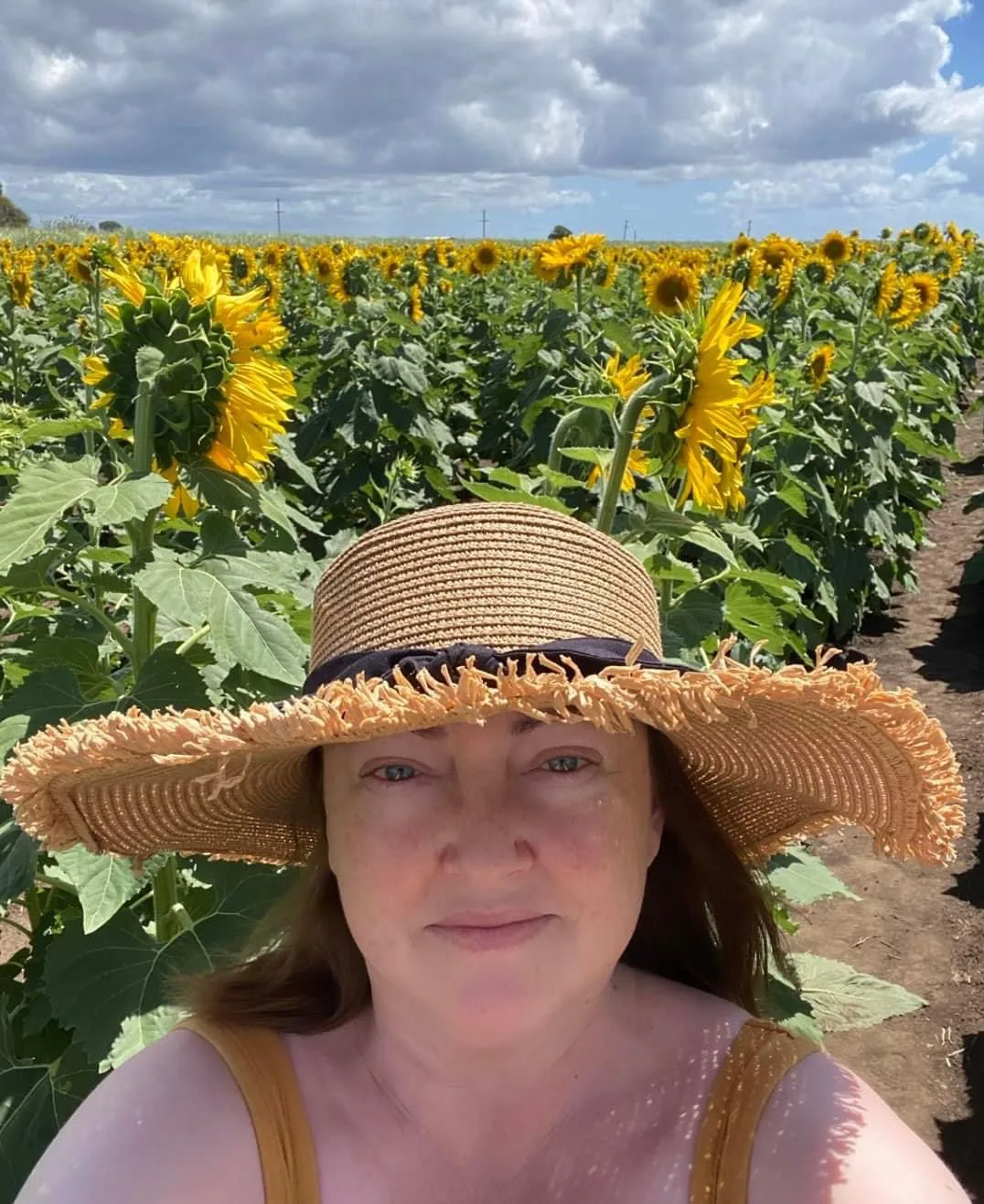 a woman standing in a sunflower field wearing a straw hat
