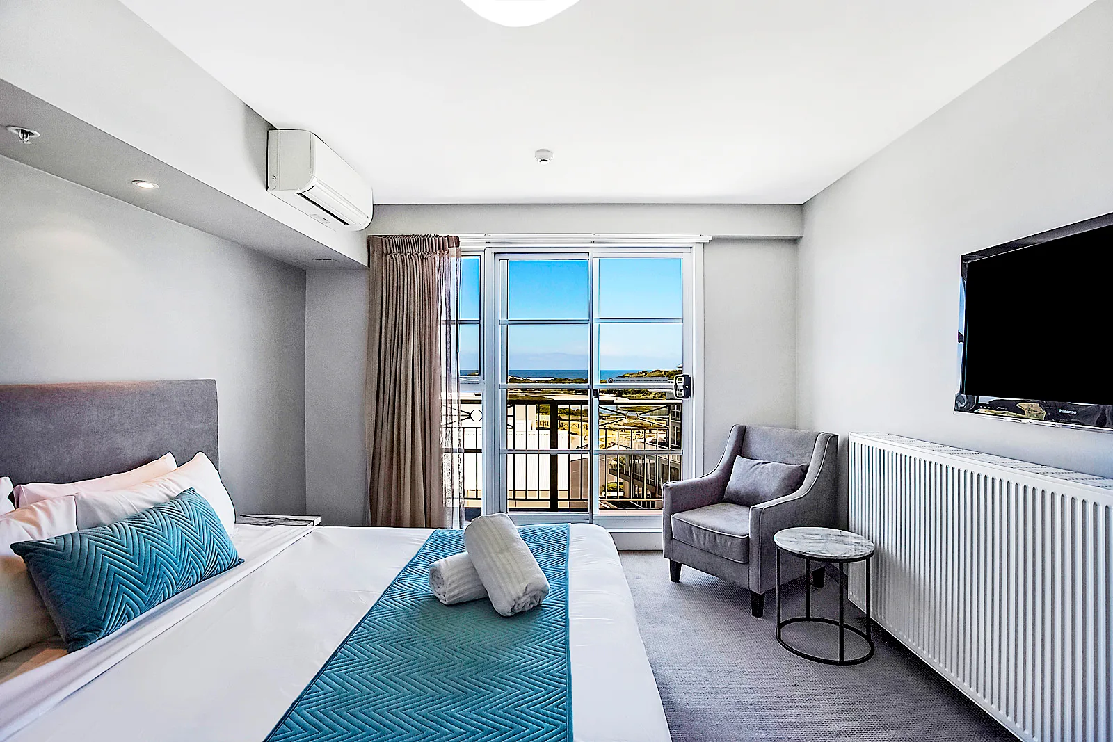 image shows the interior of a hotel room, the bed is white bed with a blue throw