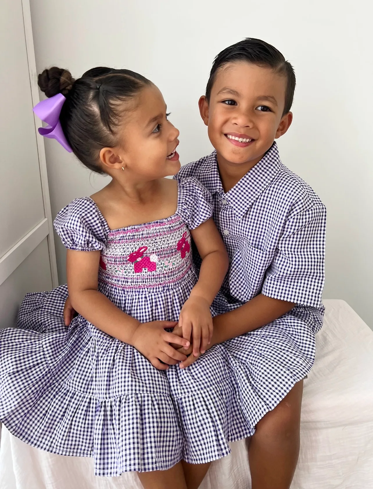 two children in navy gingham clothing, they are cuddling on a chair