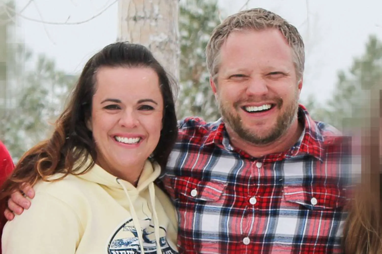 man and woman standing outside in the snow she is wearing a yellow sweatshirt and he is wearing a plaid jumper