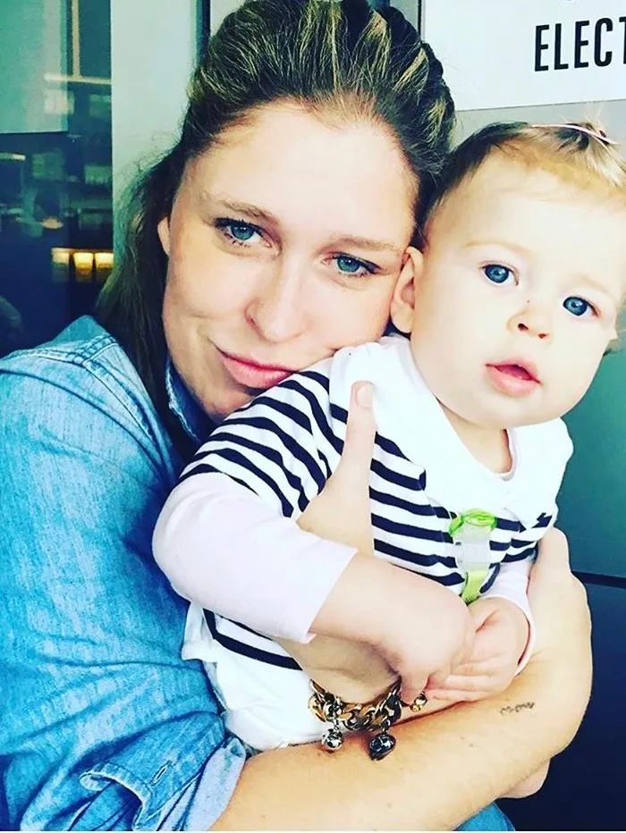 woman in blue with blue eyes holding baby in white and blue striped top