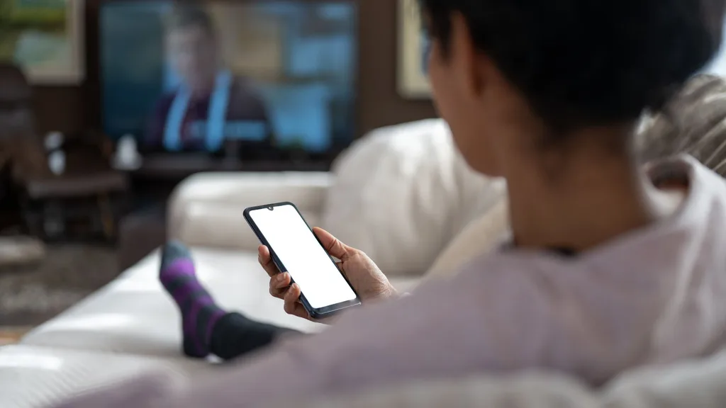 Woman on couch watching TV and phone screen