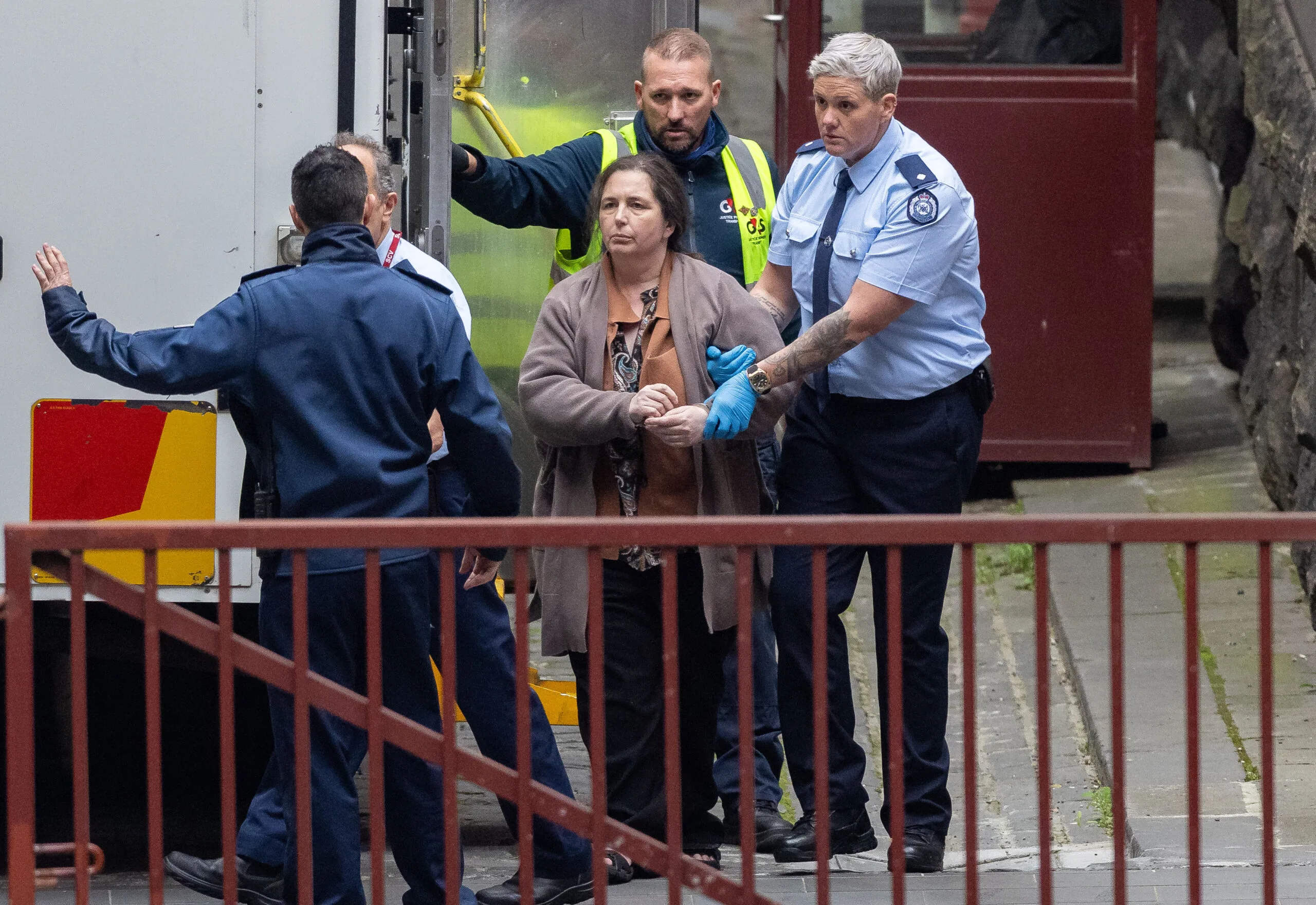 woman in gret coat being led by police 