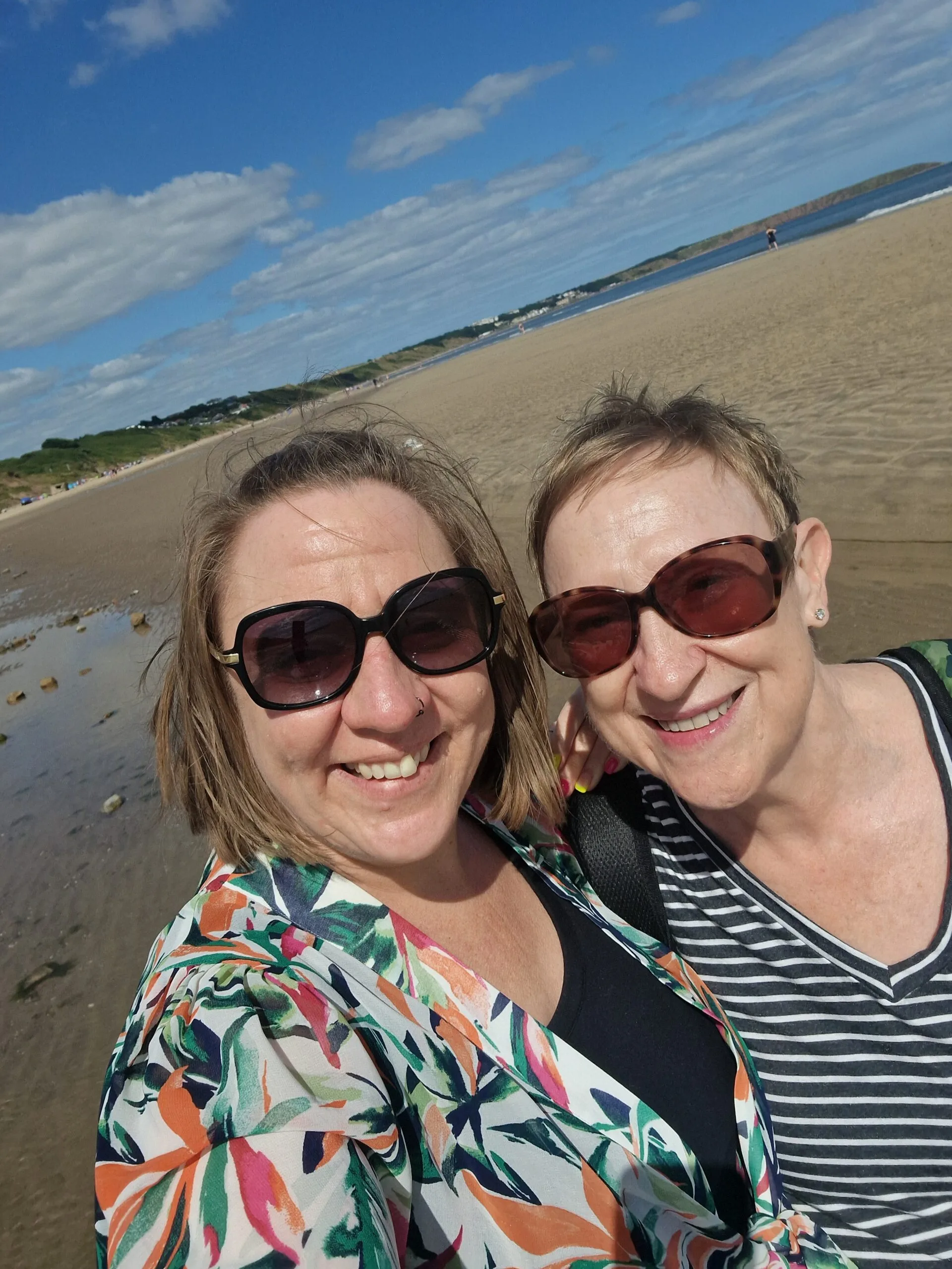 Mother and daughter smiling at camera wearing sunglasses.