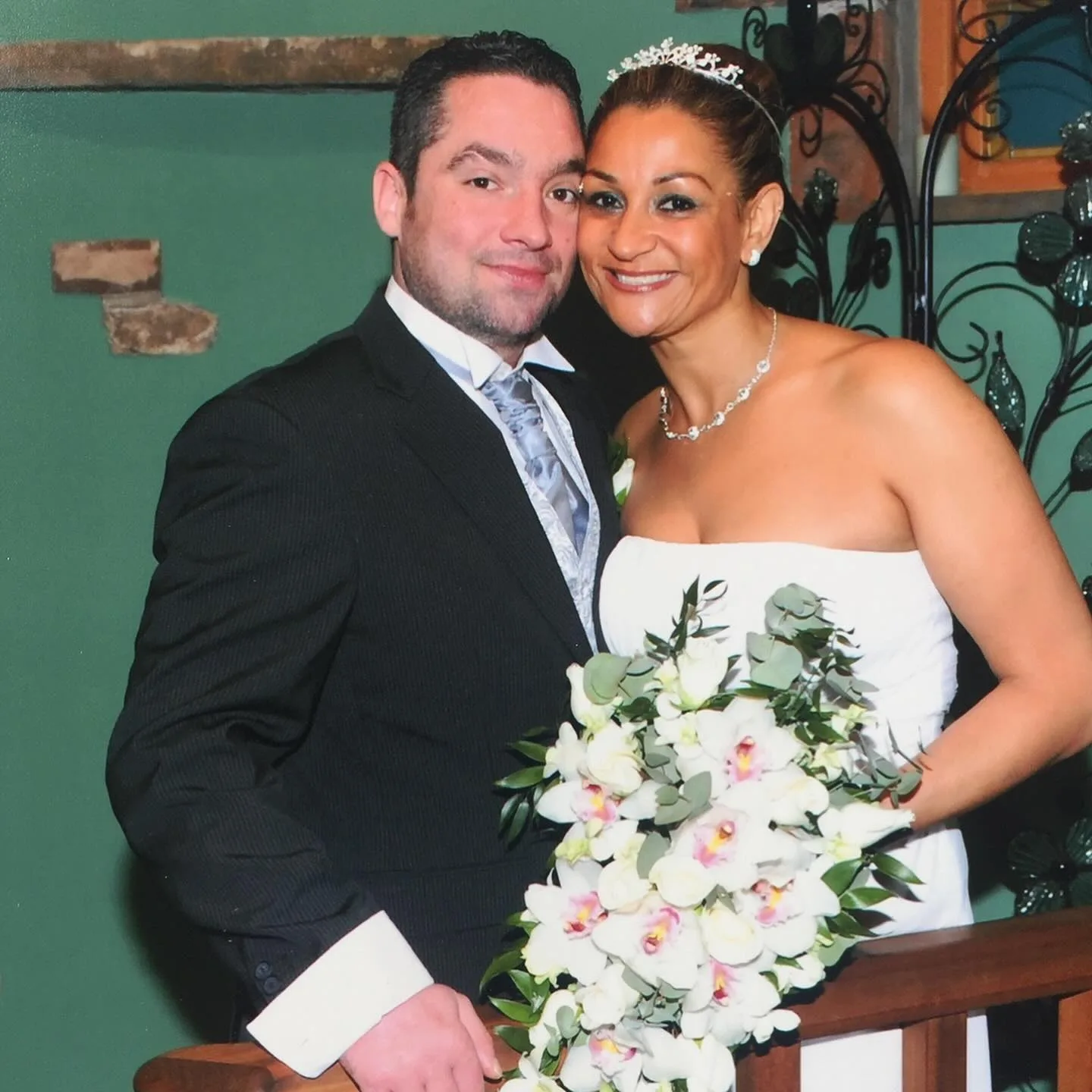 man and woman in green room standing on stairs in wedding outfit. He is wearing a suit and she is wearing a white dress
