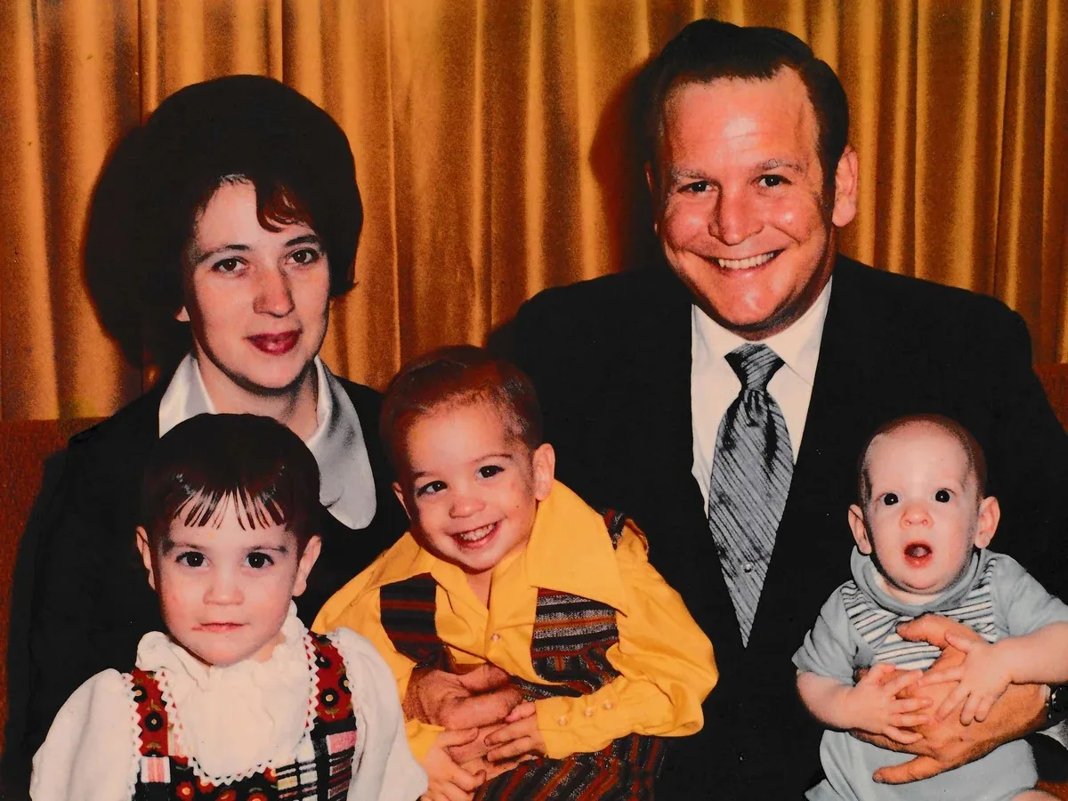 retro family photo with three children and mother and father in front of yellow curtain 