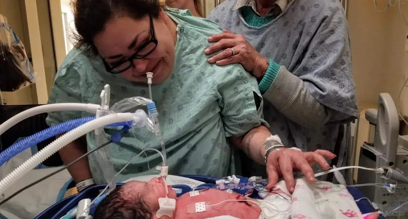 woman looking down at sick baby in a humidicrib 