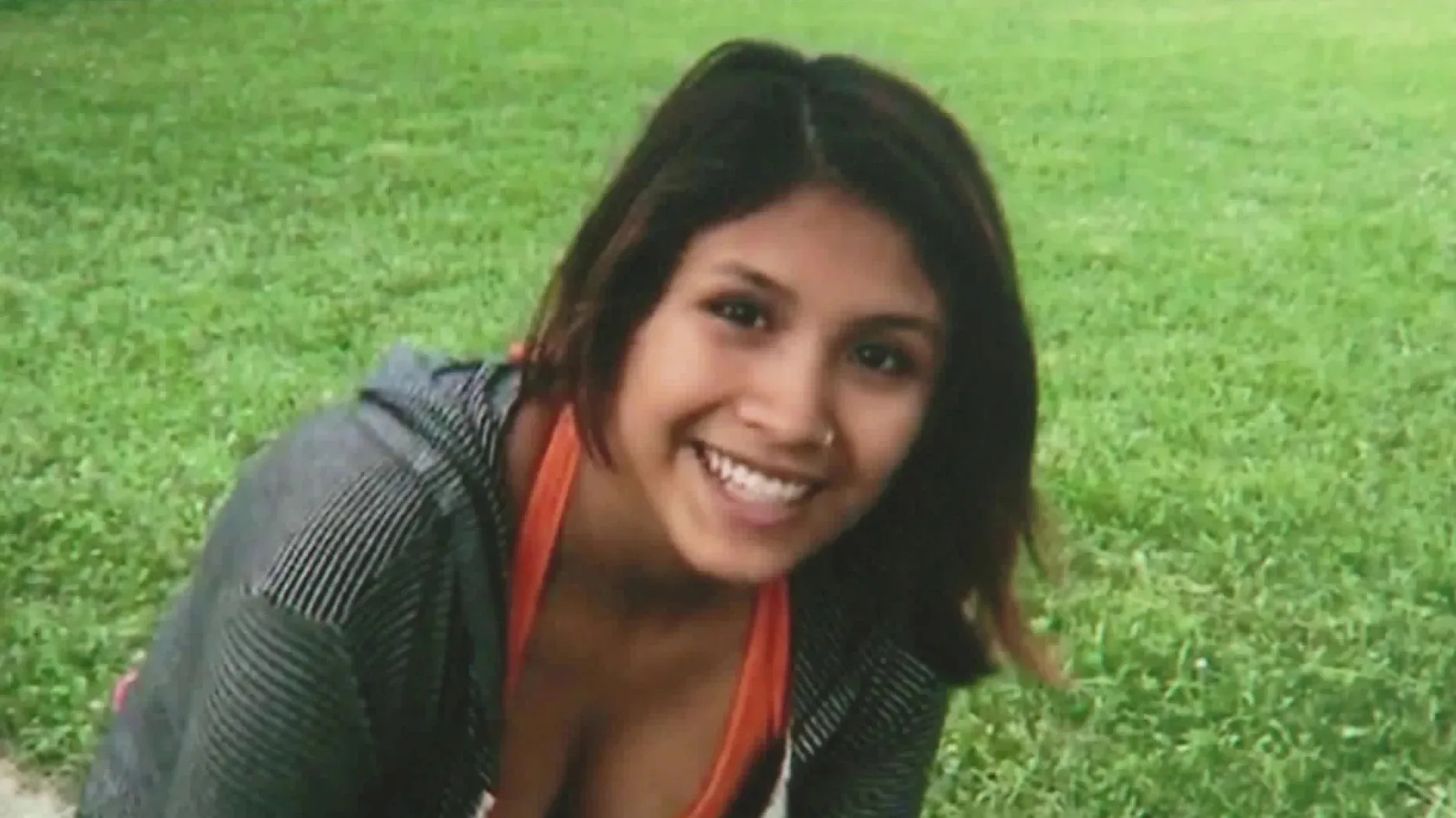 woman in a park with dark hair and features she is smiling for the camera