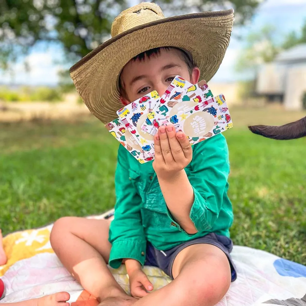 Boy holds a fan of cards in his hand sitting outside on a picnic blanket
