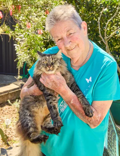 Woman wearing green shirt holding cat and smiling at camera.