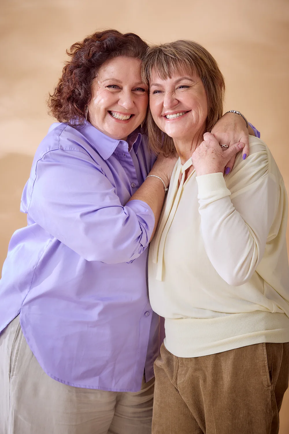 woman in purple shirt and woman in white shirt arms round each other 