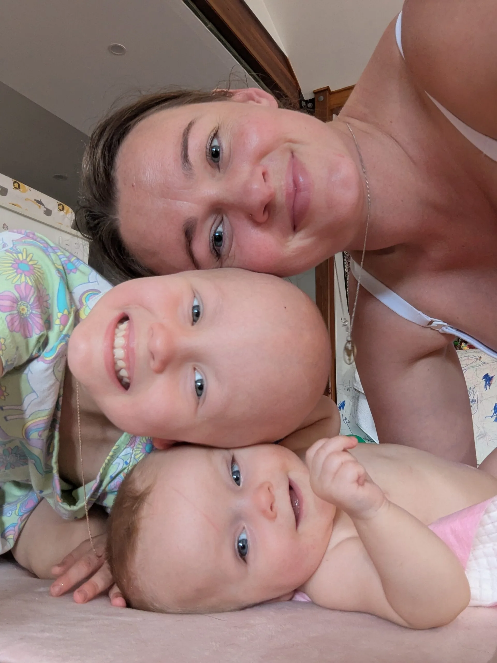 mother, younger daughter and baby with heads stacked on top of one another smiling for the camera