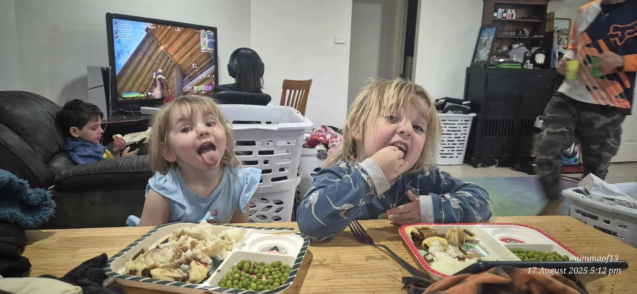 two blonde kids eating at a table with peas 