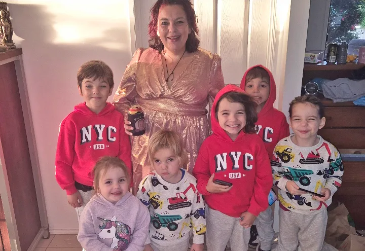 mum surrounded by kids, three are wearing NYC red jumpers and others wearing truck print shirts and one girl in a unicorn jumper 