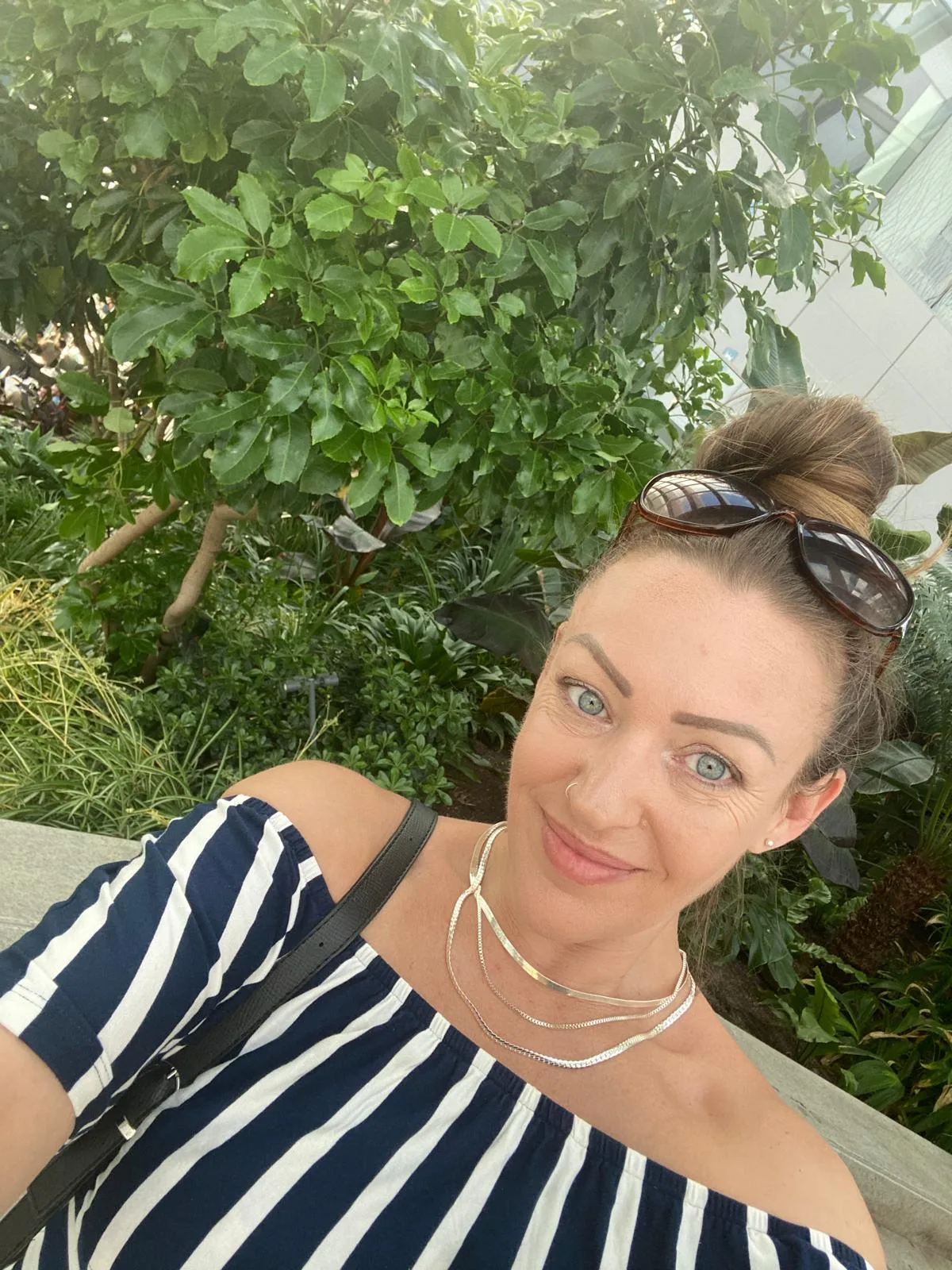 woman taking selfie outside she is wearing stripes and has glasses on her head