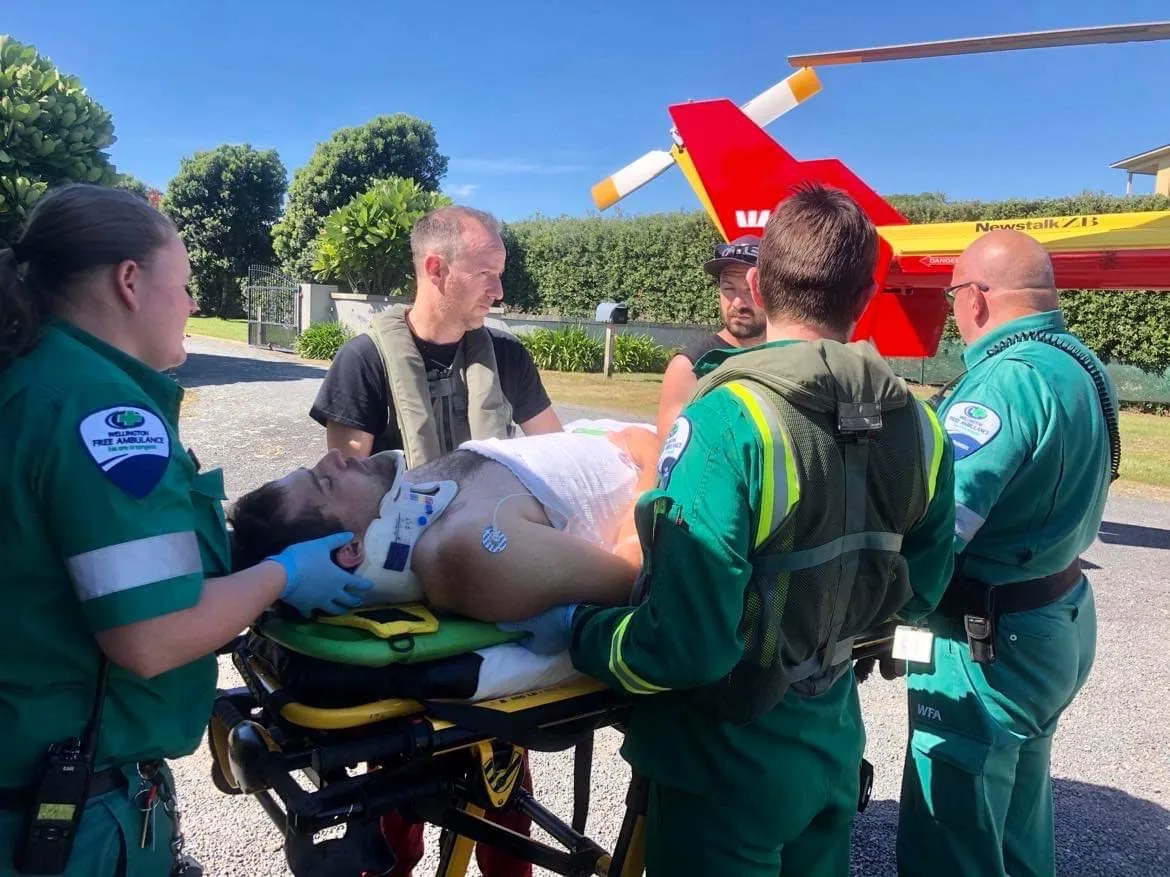 man on gurney with neck brace surrounded by four paramedics in green there is a yellow and red helicopter in the background