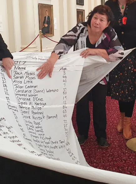 Woman standing in black and white holding roll of paper with names on on red carpert
