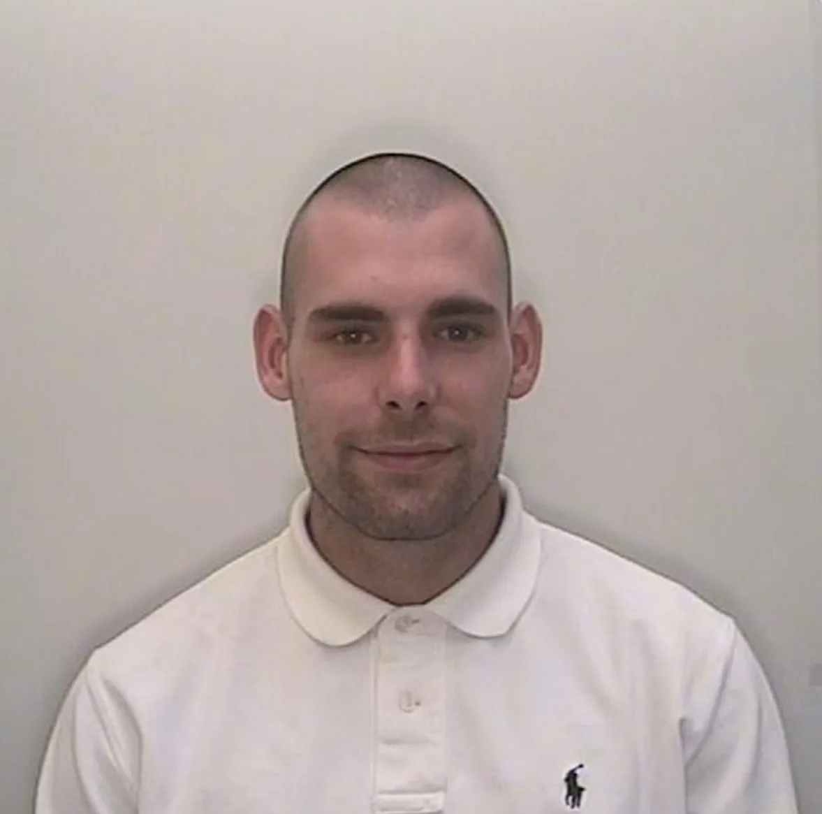 Man wearing white shirt smiling at camera in mugshot.