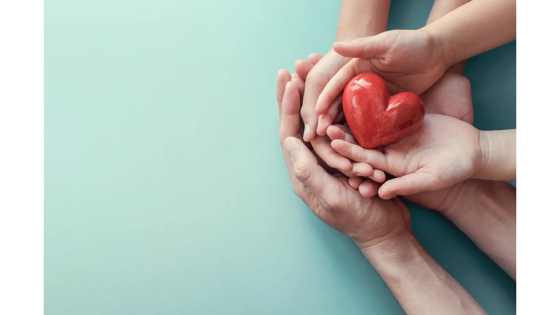 A family joins hands to cradle a red love heart.