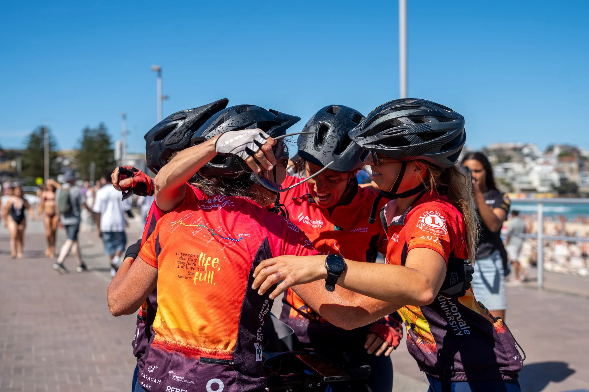 Louise and her friends in a group hug. They are wearing their riding gear and bike helmets and are at the beach.