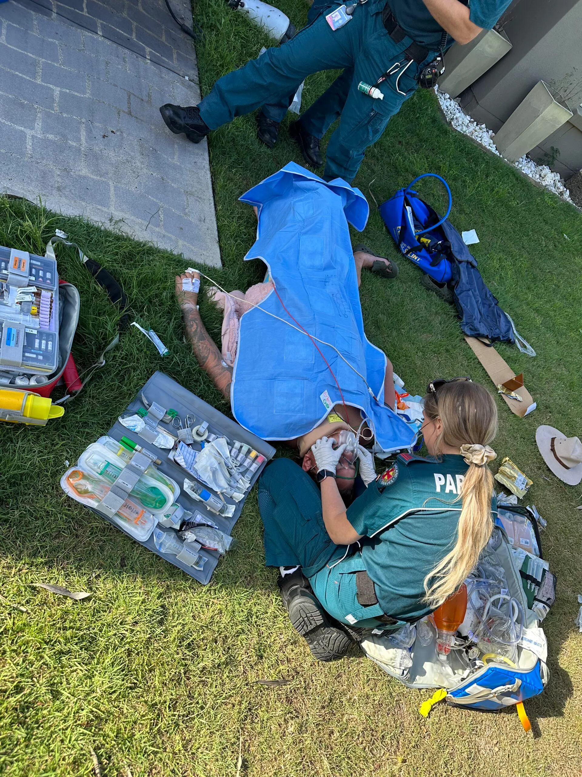 man laying on grass front yard, surronded my medics